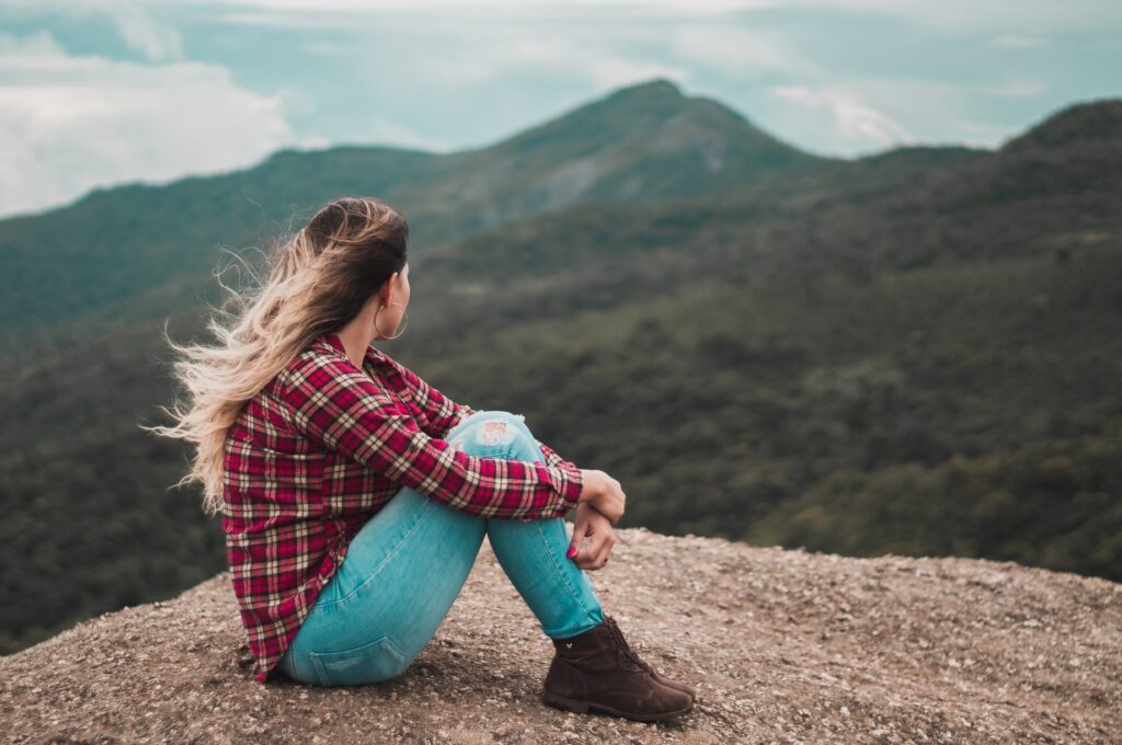 Woman pondering that is sitting on a mountain peak with a mountain range in the background