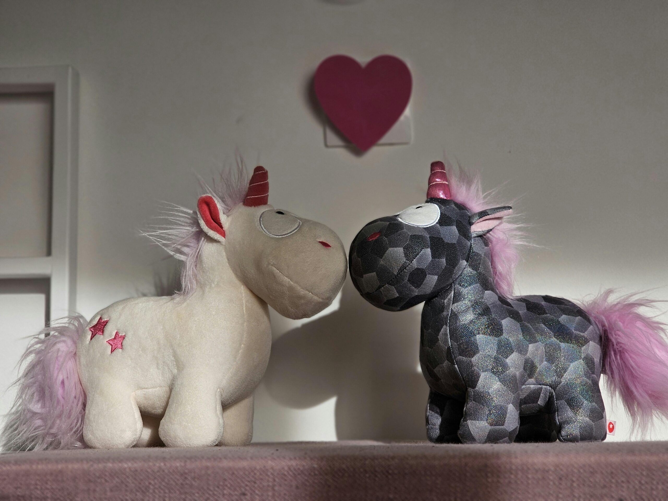 Close-up of Two Unicorn Cuddly Toys in a Room under a heart. Assumed to be boy and girl.