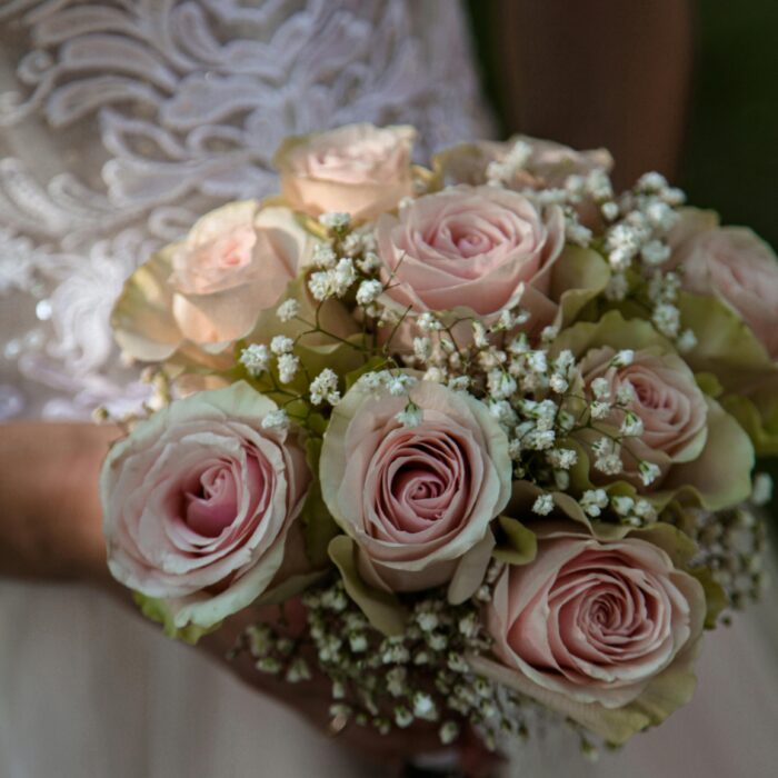 Beautiful frosty pink wedding bouquet of roses and baby breath on the bride's lap.