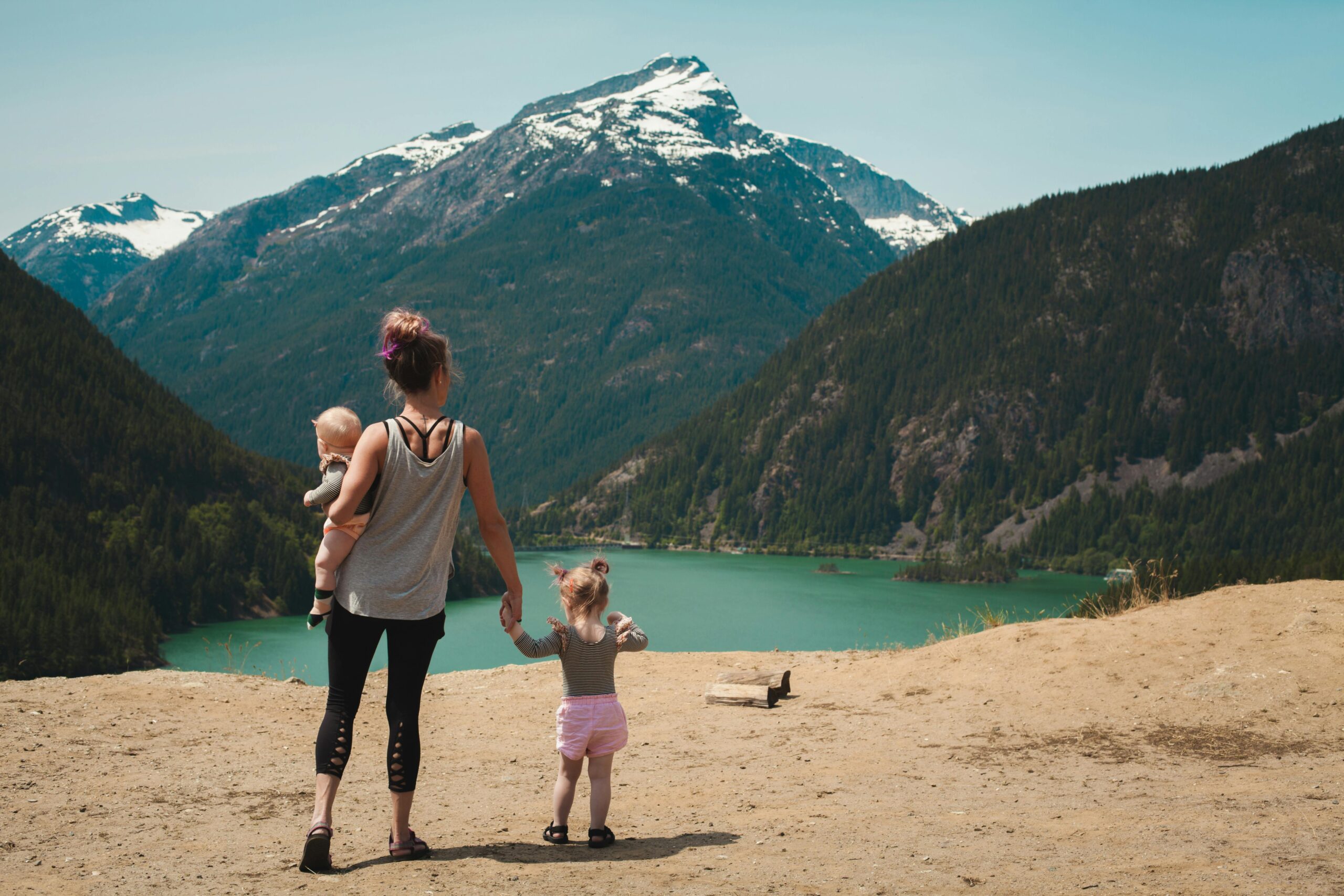 Mother and Children Walks Near Body of Water in hiking clothes with mountains in the background