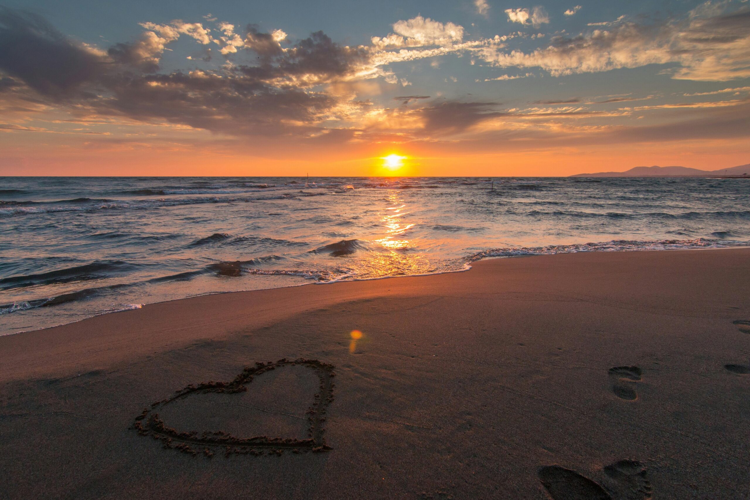 Seashore with the sunrise. On the beach a drawn heart and footprints.